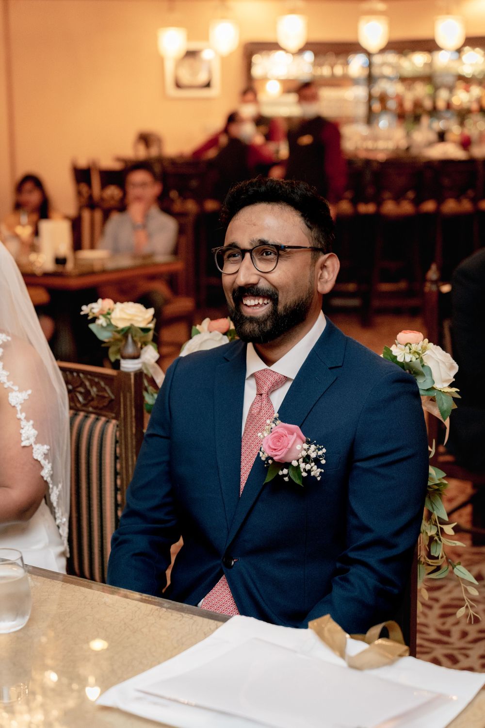 Wedding guest in navy suit with pink tie smiling during reception celebration.
