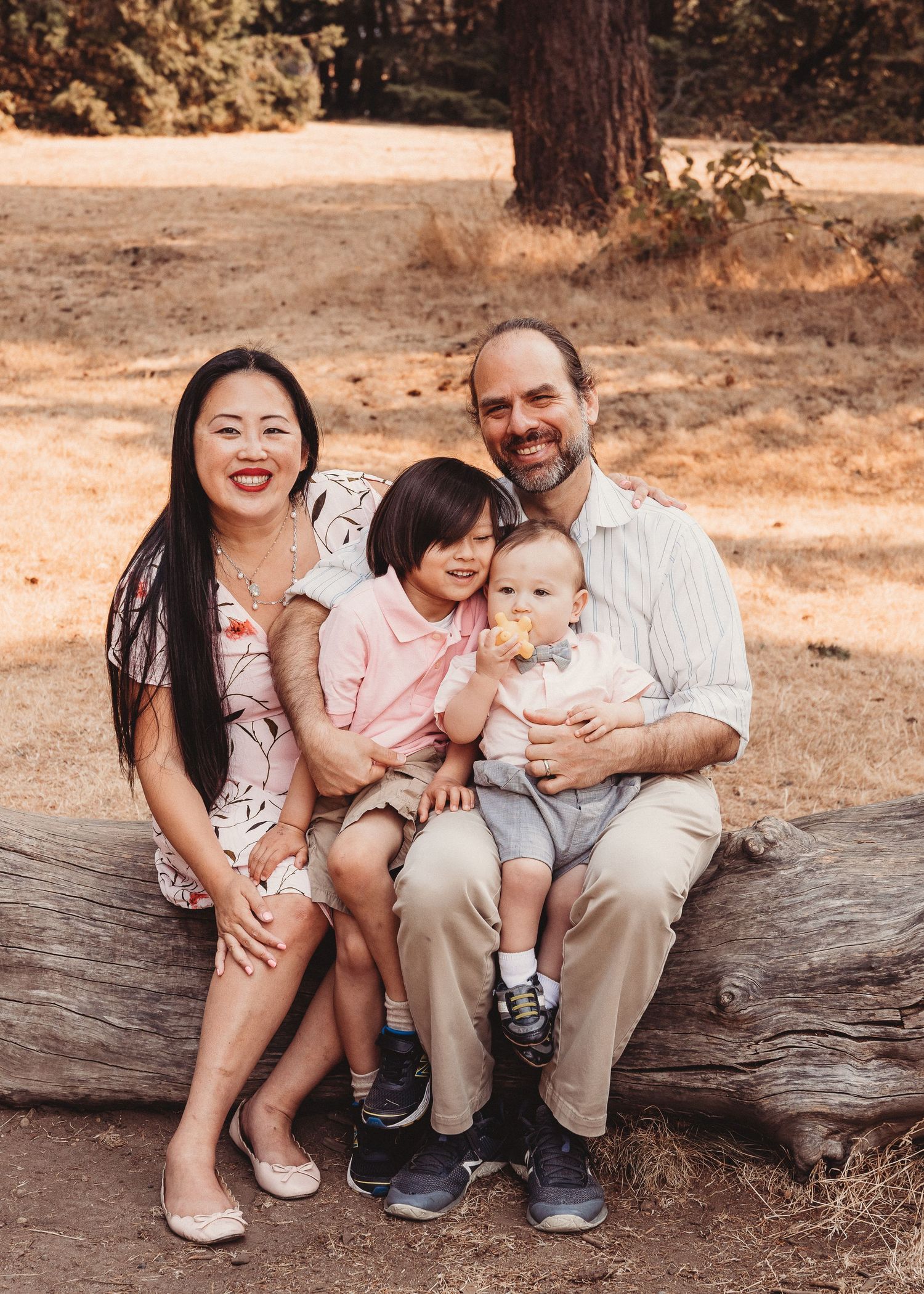 A happy family sitting together on a fallen log in a sunny forest setting.