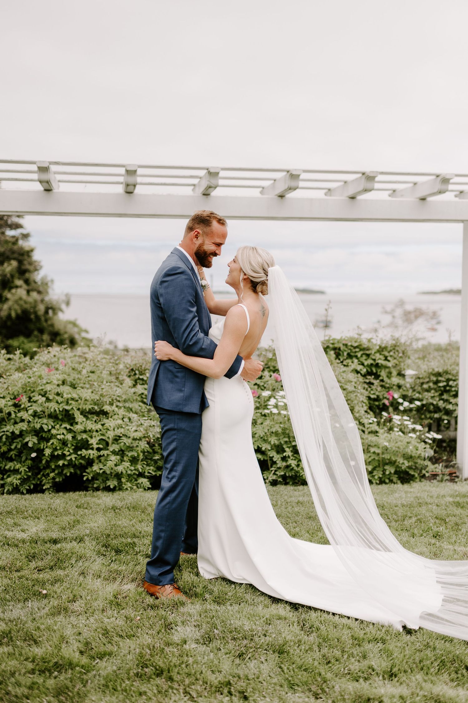 A romantic first look moment under a white pergola overlooking a scenic coastal view.