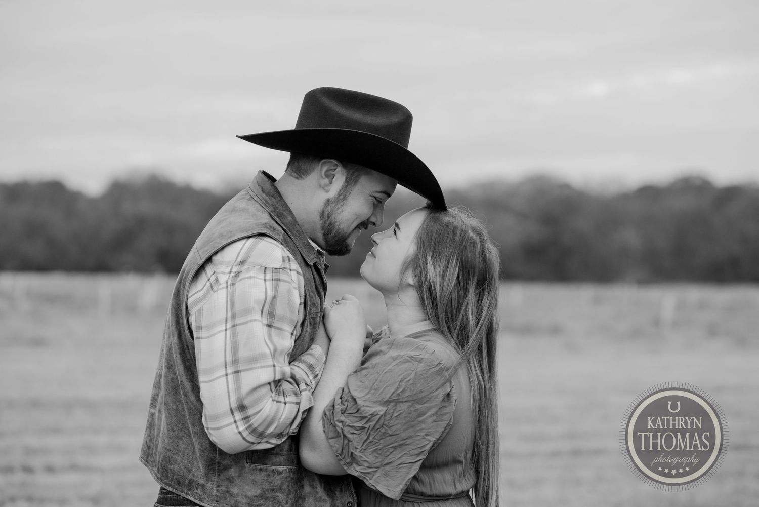 A romantic black and white portrait of a couple sharing an intimate moment in a field.