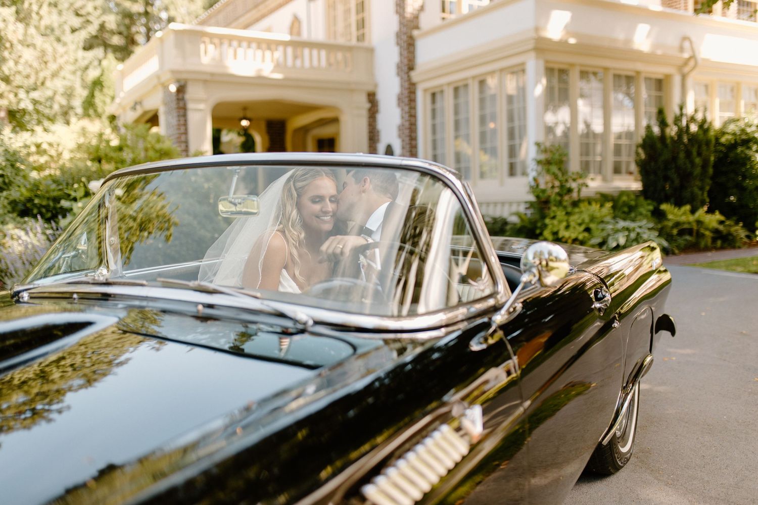 Vintage black convertible parked in front of an elegant white mansion on a sunny day.