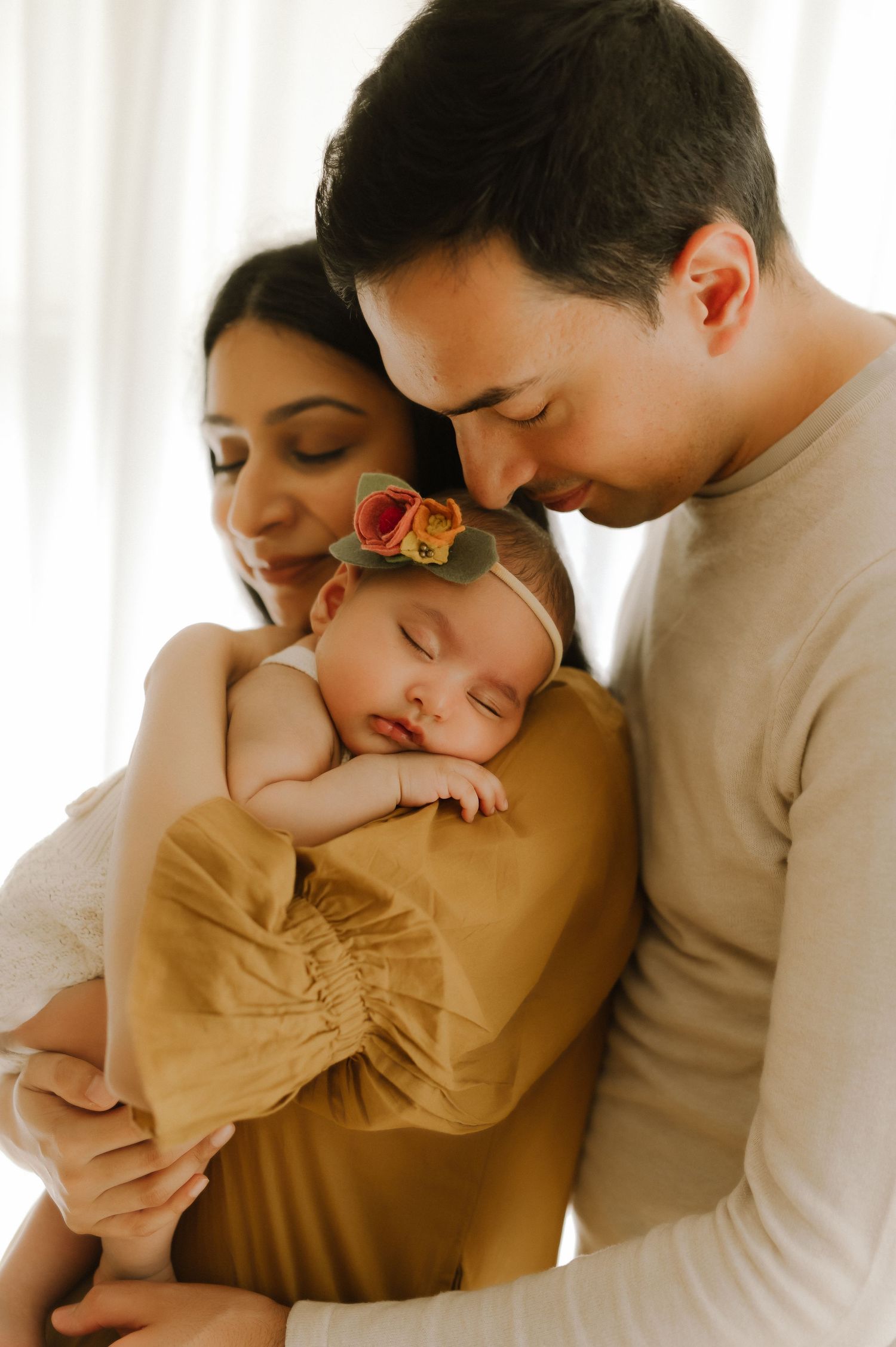 Intimate indoor family portrait with sleeping baby in warm mustard tones.