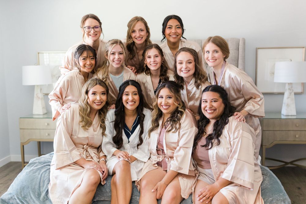 Large group in matching blush robes poses together on a bed for a special occasion photo.