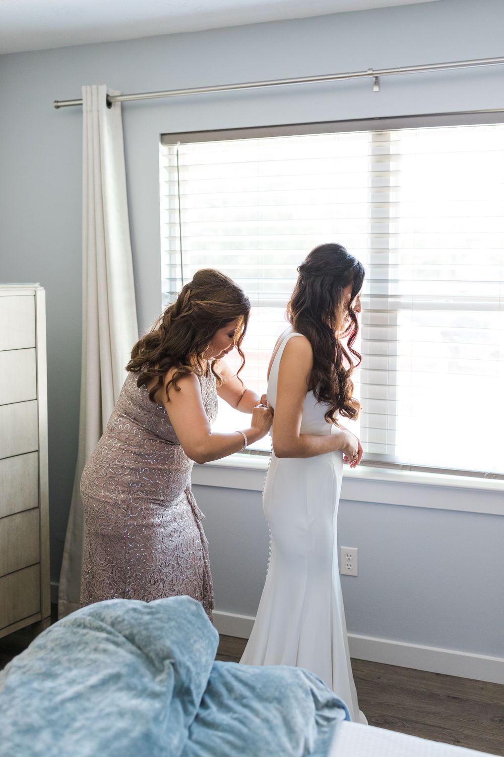 Two people stand by a window during wedding preparations, one helping with the dress.