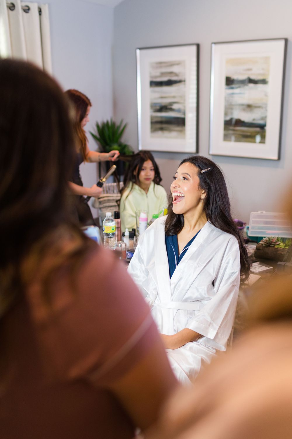 Joyful getting ready scene with women in white robes sharing laughter.