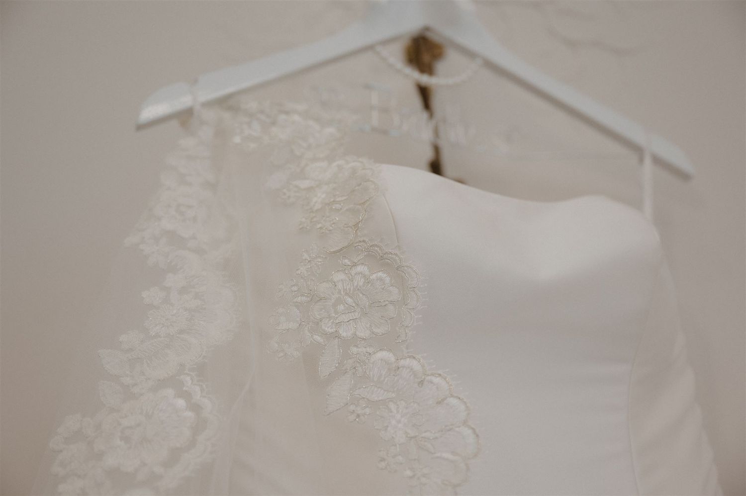 Elegant white wedding dress with delicate lace details hanging on a hanger against a neutral background.