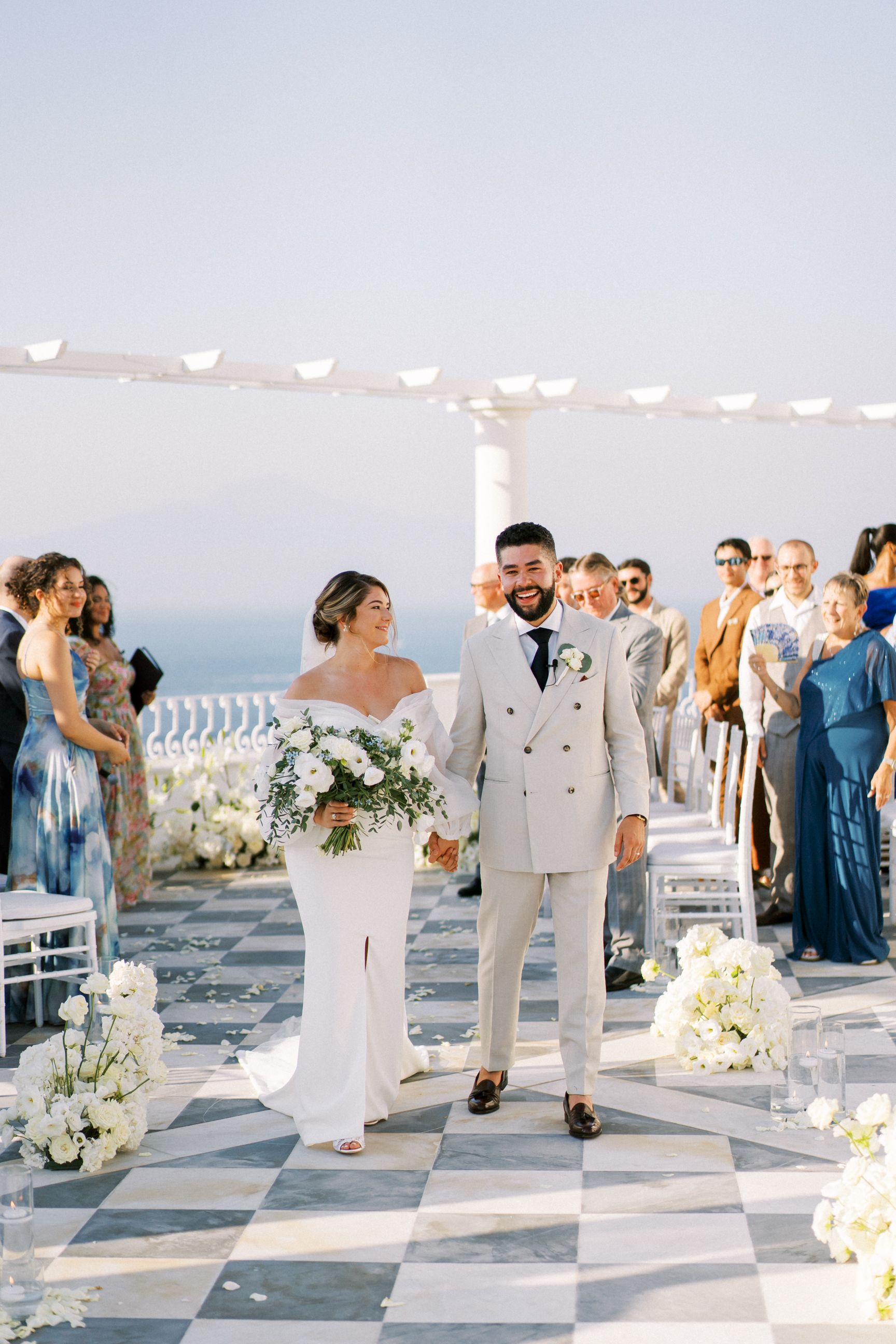 A wedding ceremony setting with checkerboard flooring and string lights overlooking the ocean.