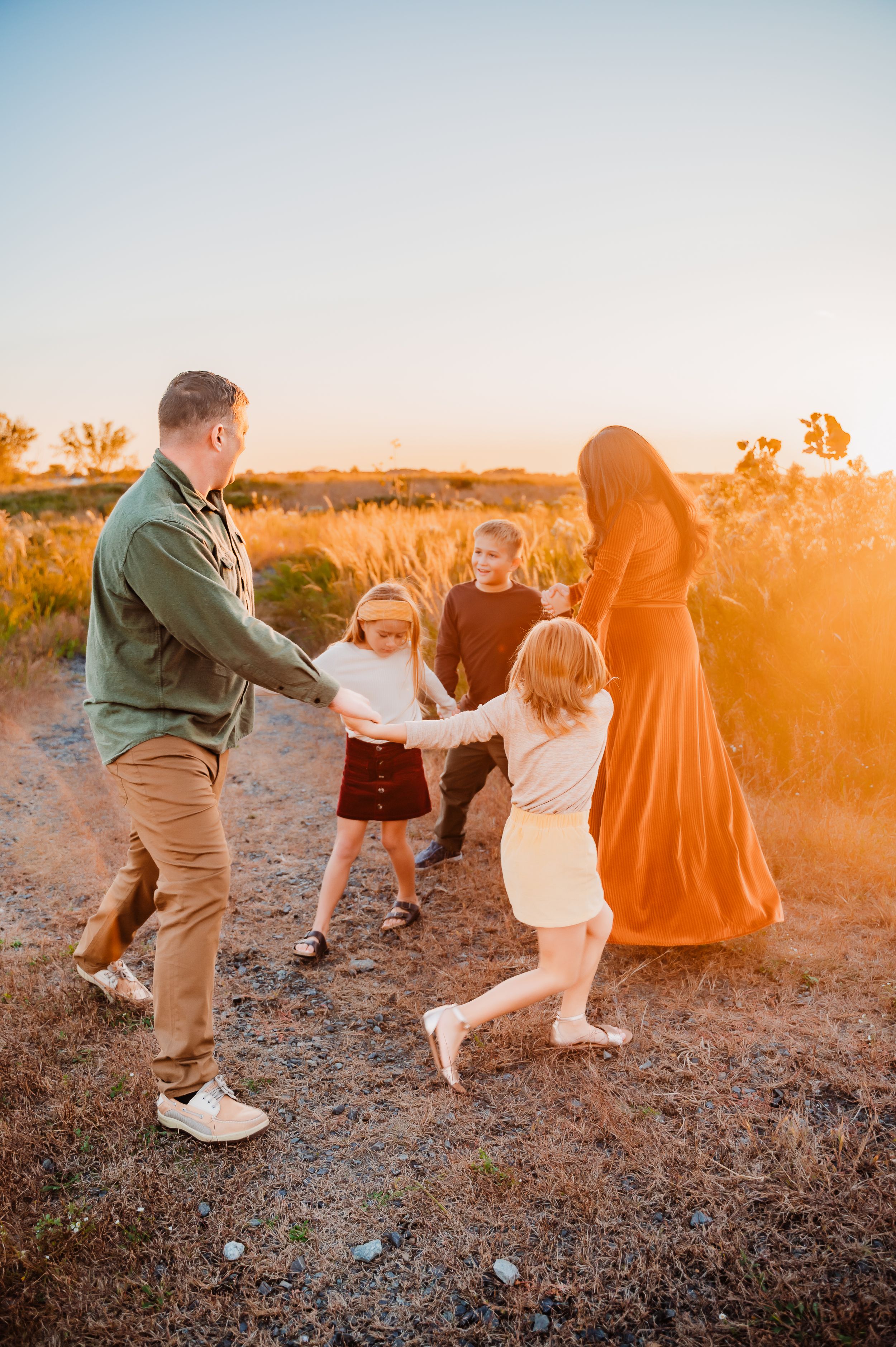 Family of 5 holding hands playing ring around the rosie in sun soaked field in Staten Island,NY