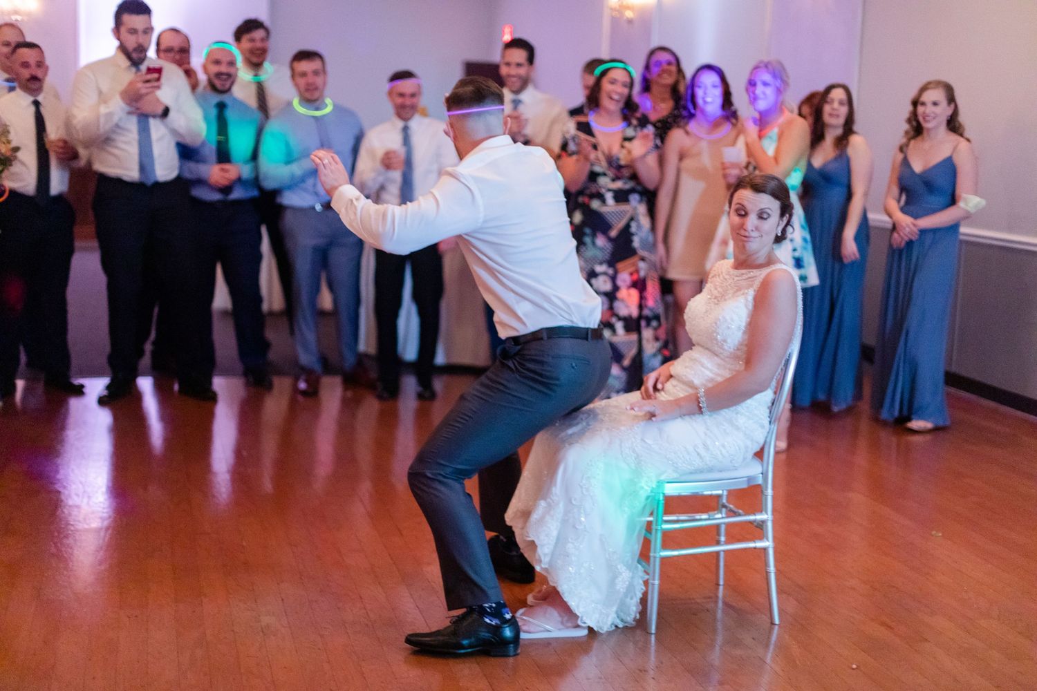 Wedding guests dancing and celebrating on a wooden dance floor at an indoor reception.