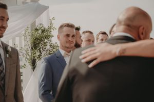 Groomsmen gather during an emotional moment at outdoor wedding ceremony.