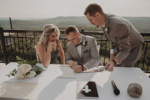 Wedding document signing moment on outdoor terrace with white floral decorations.