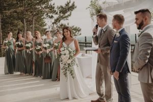 Wedding party lines up outdoors with bridesmaids in sage dresses and groomsmen in neutral suits.