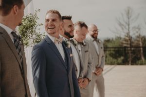 Groomsmen share a lighthearted moment while lined up during outdoor wedding ceremony.