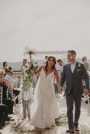 Newlyweds walking down aisle on outdoor terrace decorated with white florals.