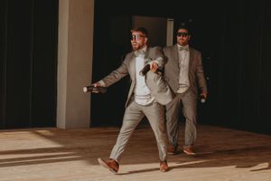 Two people dancing energetically in suits during a wedding reception.