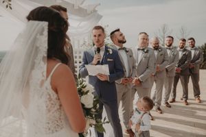 A wedding ceremony on a bright terrace with wedding party members lined up in grey suits.