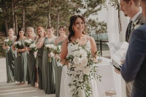 A bride in white holds a lush bouquet while bridesmaids in sage dresses line up behind her.
