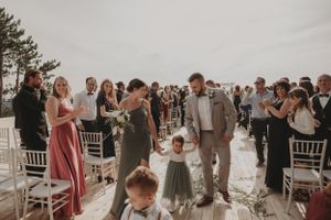 Wedding guests stand and celebrate during an outdoor ceremony with white chairs and mountain views.