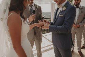 Intimate ring exchange moment during outdoor wedding ceremony with attendants looking on.