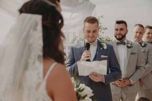 A wedding ceremony moment with bridesmaids in sage green dresses in the background.