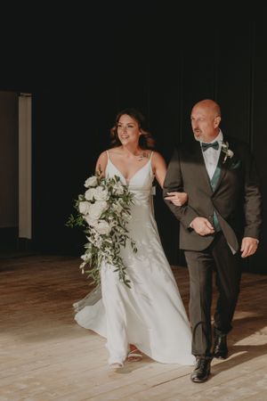 A formal procession down a wooden aisle during an indoor wedding ceremony.