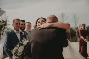 An emotional embrace shared between wedding participants during an outdoor ceremony with floral decorations.