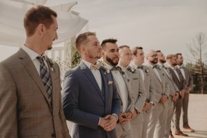 Groomsmen in coordinated suits stand in a formal line at outdoor wedding ceremony.