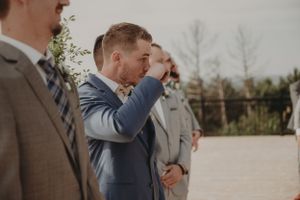 Groomsmen stand in a row wearing suits in varying shades of grey and brown.