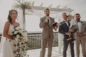 An outdoor wedding ceremony under a white pergola with floral decorations.