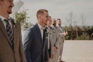 Groomsmen in suits of varying shades of grey and brown stand together outdoors.