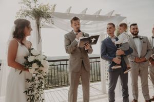 A wedding ceremony takes place on an outdoor terrace with white decor and floral arrangements.
