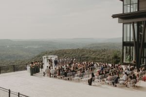 Aerial view of mountain wedding venue with white chairs and ceremony arch on outdoor deck.