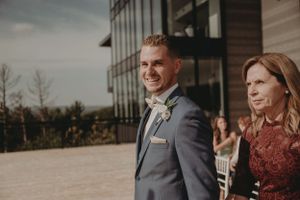 Couple stands outdoors in formal attire with modern building and landscape in background.