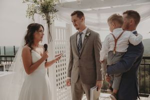 A wedding ceremony exchange on an outdoor terrace with white decor and floral arrangements.