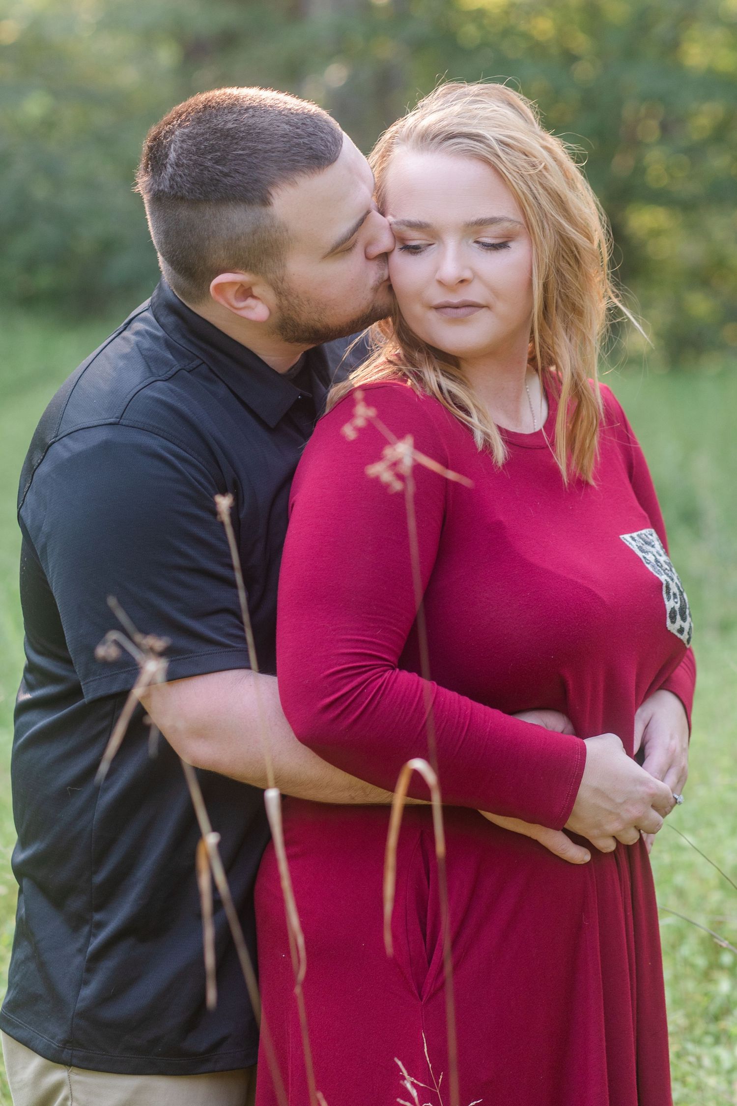 Couple sharing an intimate moment in a sunlit field wearing red and black outfits.