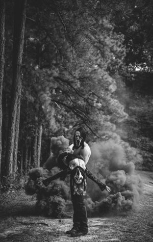 Masked figures in a wooded area with dramatic smoke effects creating an eerie Halloween atmosphere.