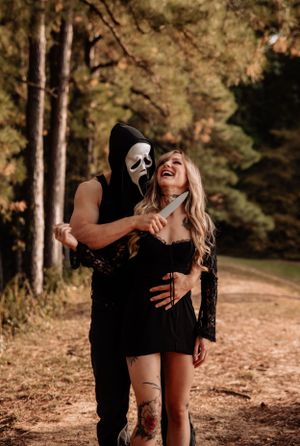 A couple in black clothing pose dramatically in a wooded forest setting during an autumn photoshoot.