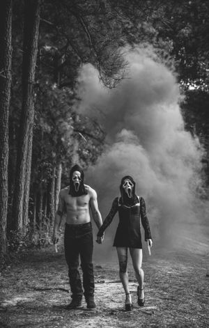 Atmospheric forest photoshoot with smoke effects and dark figures walking among tall trees.
