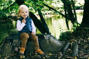 Child sitting thoughtfully on a tree stump beside a serene forest stream.