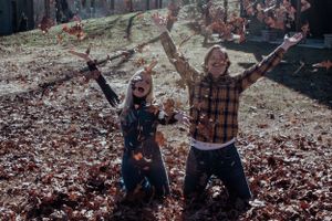 Two people playing in fallen autumn leaves while raising their arms joyfully.