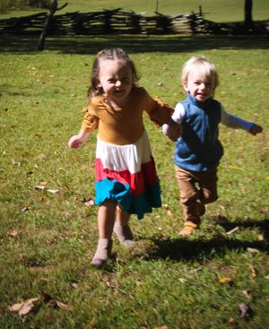 Two children running playfully through a grassy field on a sunny afternoon.