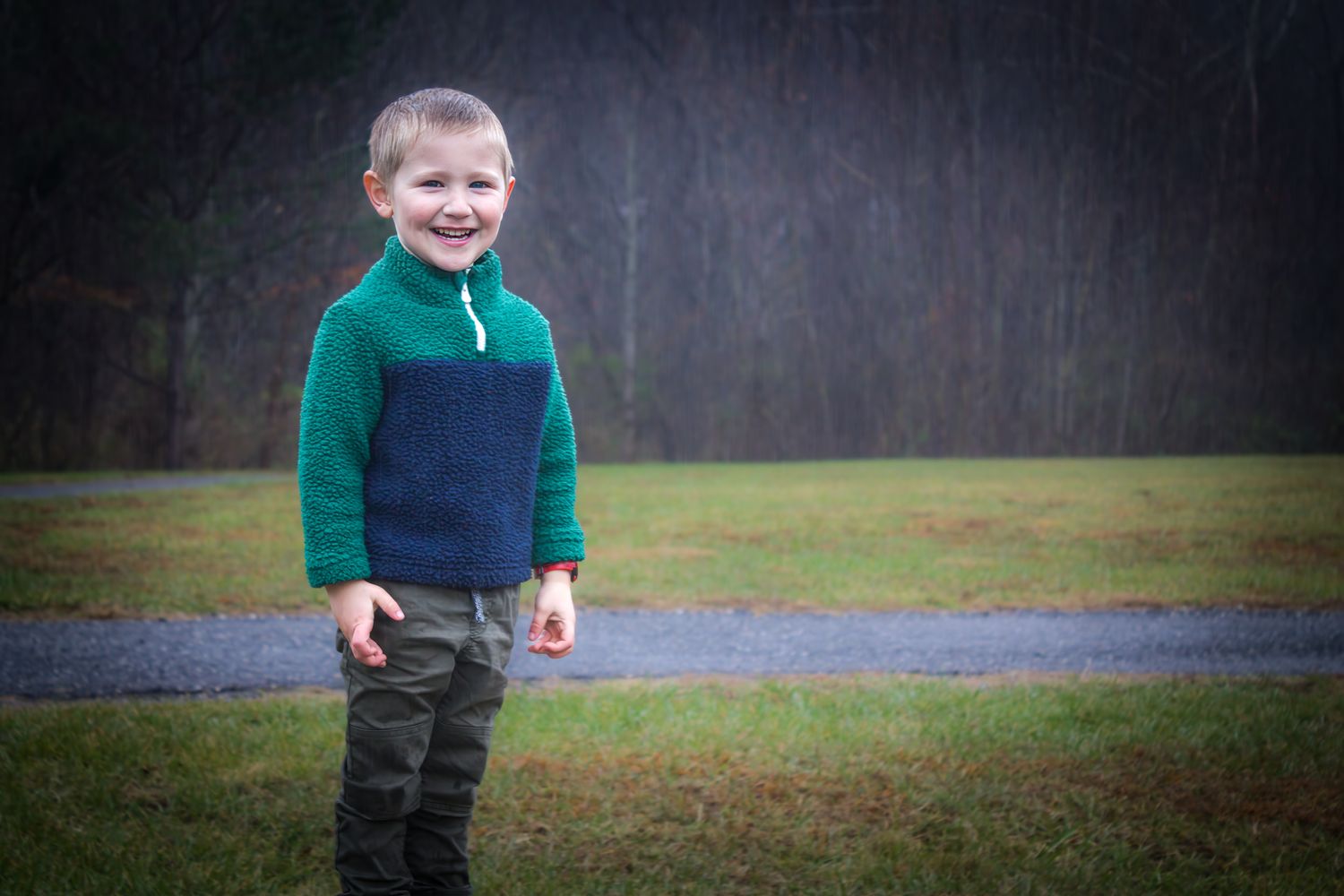 Young person in a green and navy fleece standing outdoors on a cloudy day.
