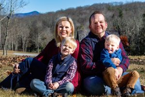 A family of four sits together on fallen leaves with mountains in the background.