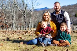 A family poses together on autumn ground with bare trees and mountains behind them.