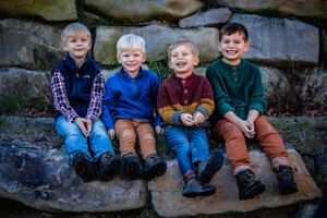 Four children sit together on stone steps wearing colorful sweaters and smiling.
