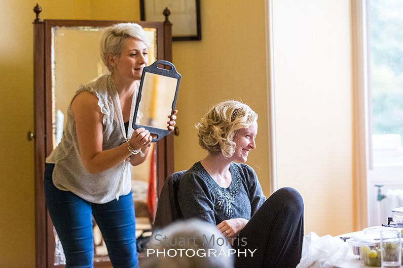 hairdresser holds up a mirror to show the bridesmaid the back of her hair