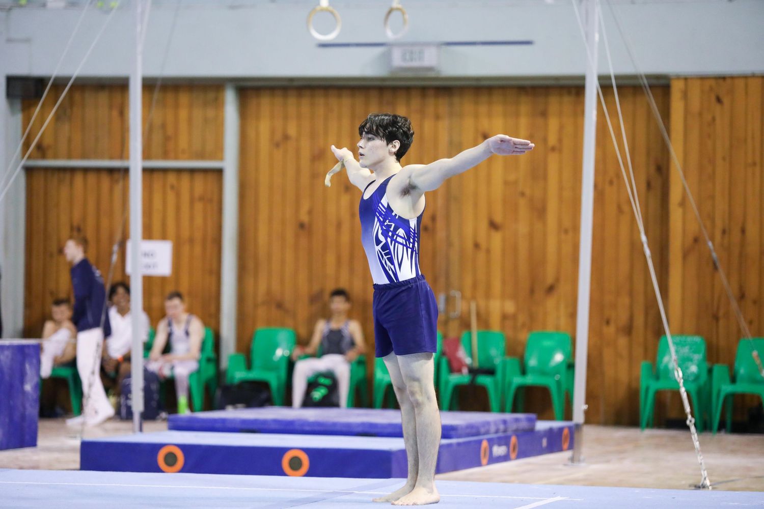 Gymnast performs graceful balance beam routine in competition setting with spectators.