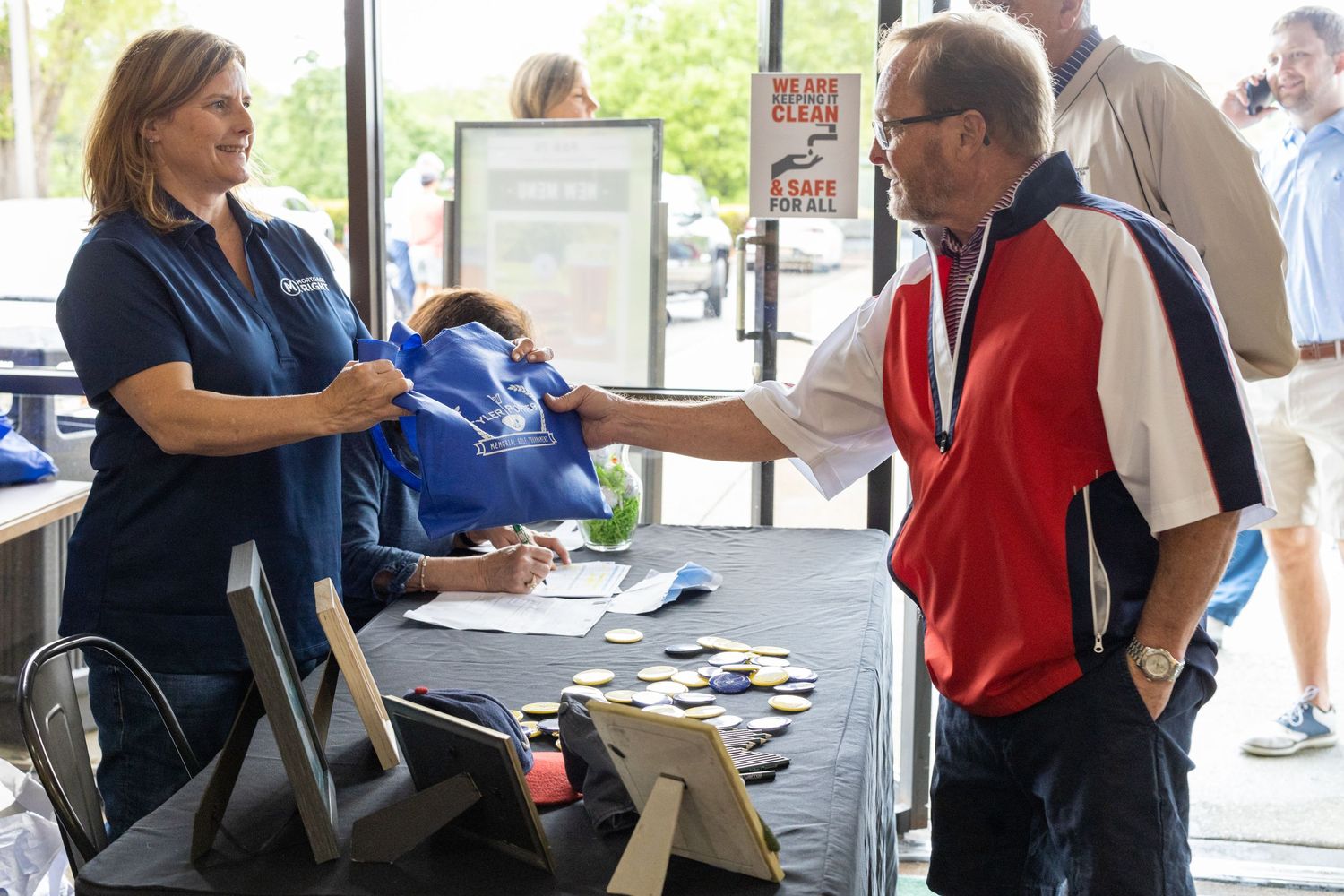 Staff member hands out blue bags at event registration table.