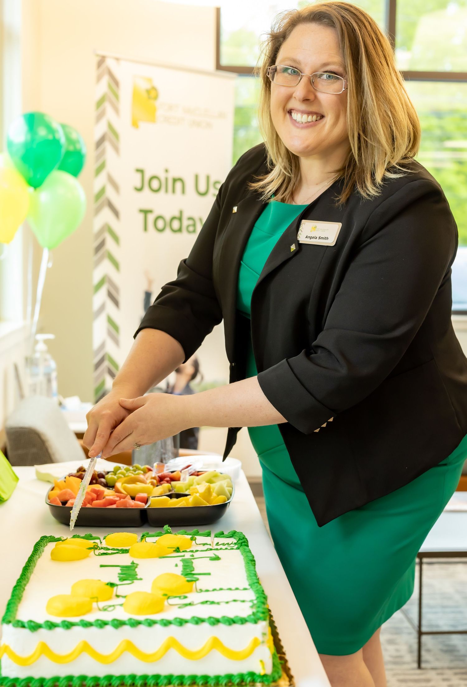 Decorated cake serving station with green and yellow themed desserts and balloons for a celebration.