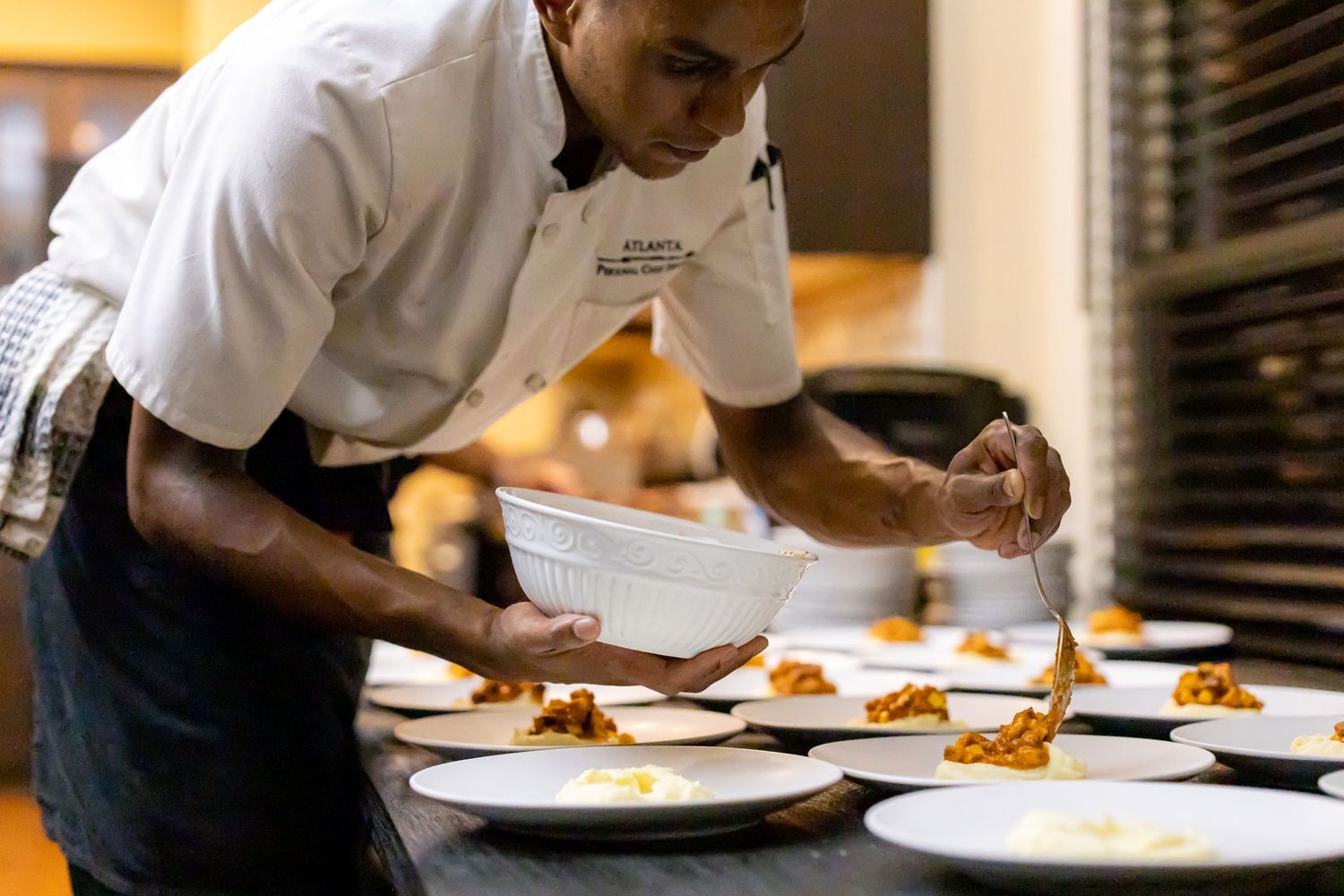 Chef in white uniform carefully plating dishes in a restaurant kitchen.